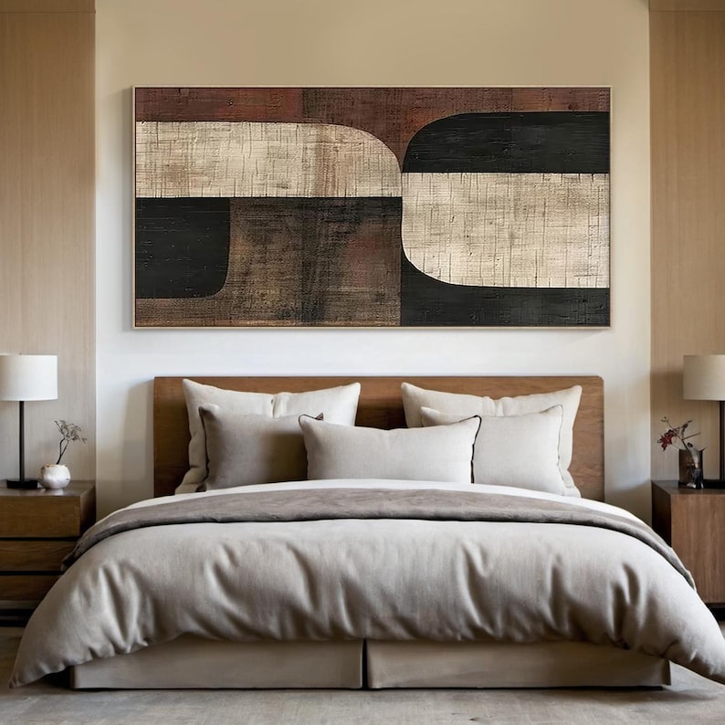 May include: Abstract geometric painting with brown, black, and white shapes. The painting is hanging above a bed with a beige headboard and a gray duvet.