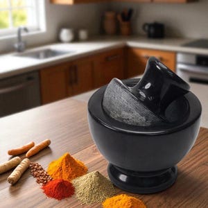 Peut inclure: Un mortier et pilon noirs avec une base arrondie et un pilon incurvé. Diverses épices, dont du curcuma et du piment en poudre, sont disposées sur une surface en bois à côté du mortier.