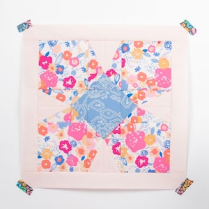 Puede incluir: Un bloque de colcha rosa y blanco con un patrón floral, una máquina de coser y una pila de recortes de tela en varios tonos de rosa y naranja.