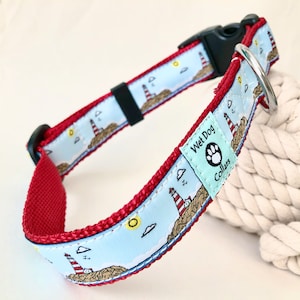 May include: Red dog collar with a blue and white lighthouse pattern. The collar has a black buckle and a silver D-ring. The collar is labeled "Wet Dog Collars".