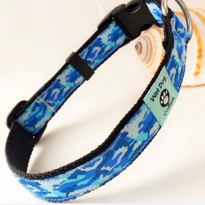 May include: Blue and white camouflage dog collar with black edging and a black buckle. The collar has a light blue tag that says "Wet Dog Collars".