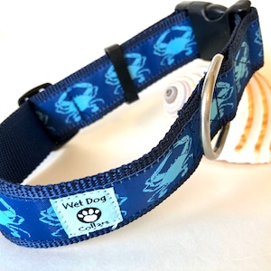 May include: Blue dog collar with a blue crab pattern and a black buckle. The collar has a white tag that says "Wet Dog Collars" with a paw print.