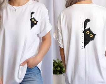 May include: White t-shirt featuring a black cat graphic peeking from the side. The cat has yellow eyes and a fluffy appearance. The back of the shirt has the text "I SEE EVERYTHING" vertically aligned next to a similar cat graphic.