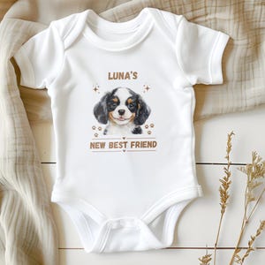 May include: White baby onesie with a brown, black, and white puppy illustration. The onesie has the text "Luna's New Best Friend" printed on it.
