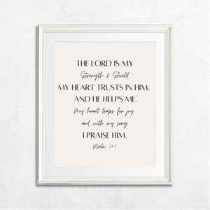 May include: A white framed print with a black and white text design. The text reads "The Lord is my Strength & Shield. My heart trusts in Him, and He helps me. My heart leaps for joy, and with my song I praise Him. Psalm 21:7"