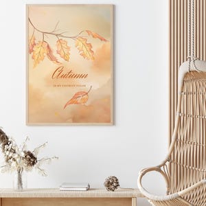 Op de afbeelding: Een ingelijste aquarelprint met herfstbladeren in oranje en gele tinten. Het kunstwerk bevat de tekst "Autumn is my favorite color" in elegant schrift. De print wordt gepresenteerd in een lichtgekleurde houten lijst.
