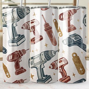 May include: A white tumbler featuring a repeating pattern of vintage-style power drills in shades of blue, brown, and red. The design includes gold-colored star accents and tool-shaped elements, creating a construction-themed aesthetic.