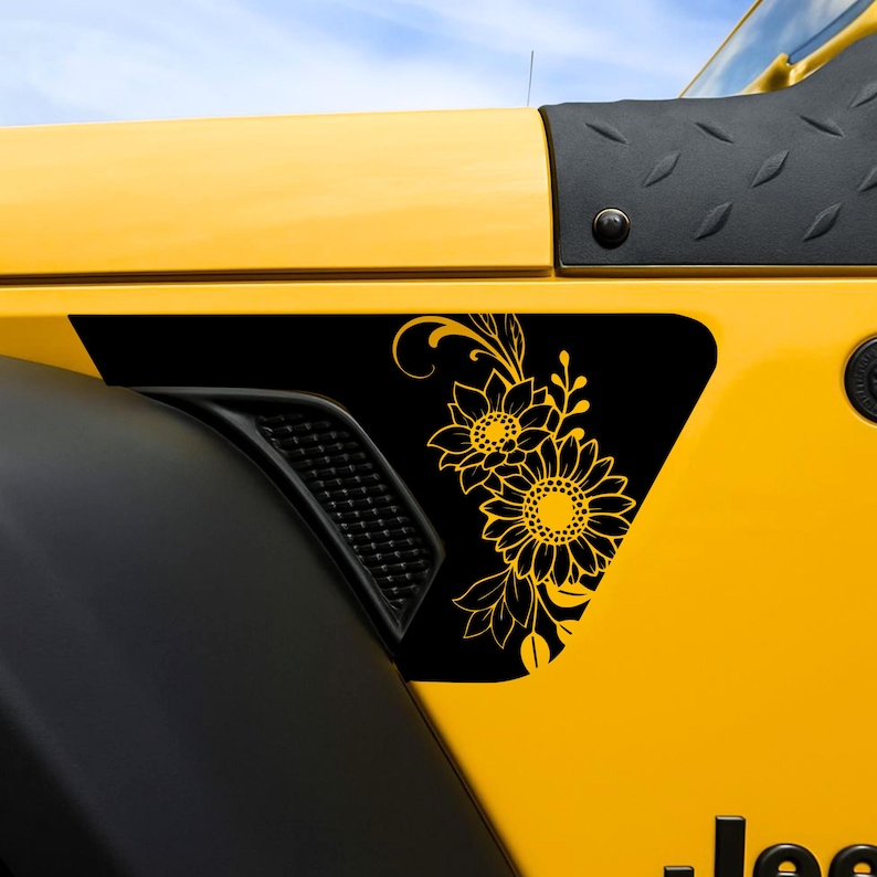 以下が含まれることがあります： 金色のヒマワリのデザインが施された黒いパネルが付いた黄色の車両。ヒマワリのグラフィックには、2つの大きな花と葉が含まれています。車両の黒いフェンダーと通気孔が見えます。