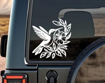Puede incluir: Calcomanía de vinilo blanco de un colibrí con su pico en una flor. El colibrí y la flor están delineados en un estilo simple y elegante.