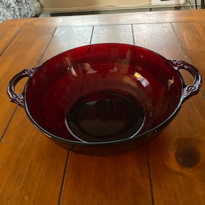 May include: A red glass bowl with two handles. The bowl has a textured surface and is empty.
