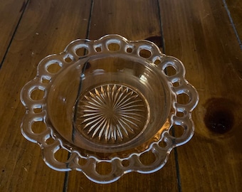 Pode incluir: Uma tigela de vidro transparente com uma borda festonada e um tom rosado. A tigela tem um padrão decorativo de sol no fundo.