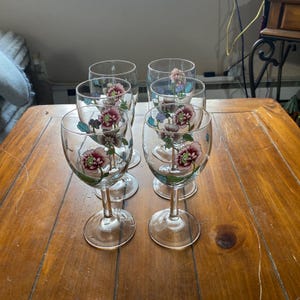 Puede incluir: Juego de seis copas de vino de vidrio transparente con diseños florales. Las copas tienen un tallo delicado y una copa redonda. Las flores están pintadas en tonos de rosa, azul y verde.