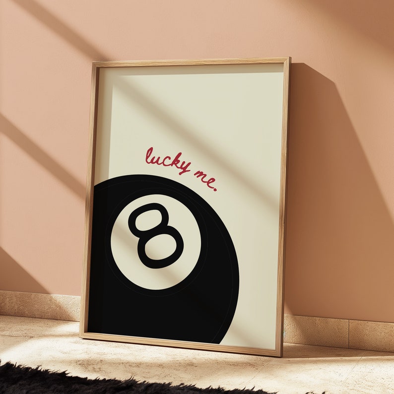 May include: A framed print with a black and white illustration of a pool ball with the number eight on it. The text "lucky me." is written in red cursive above the ball.