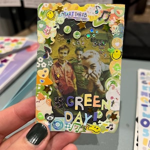 May include: A colourful card featuring a photo of the band Green Day, surrounded by stickers and glitter. The card reads "Heart Throb" and "Green Day!" in colourful lettering.