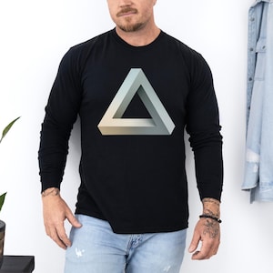 May include: Black long-sleeve shirt featuring a 3D impossible triangle graphic in shades of gray and beige. The shirt is made of a soft material and has a crew neck. A casual, everyday wear top.