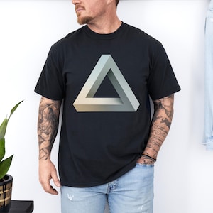 May include: A black short-sleeved t-shirt featuring a large, centered graphic of a Penrose triangle. The geometric shape is rendered in shades of light gray, white, and soft beige, creating an optical illusion of a three-dimensional object.