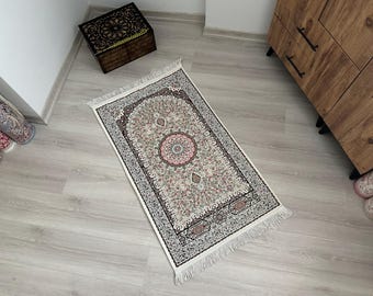 May include: A white prayer rug with a floral pattern in shades of pink, beige, and brown. The rug has a fringe border and is made of a soft, luxurious fabric.