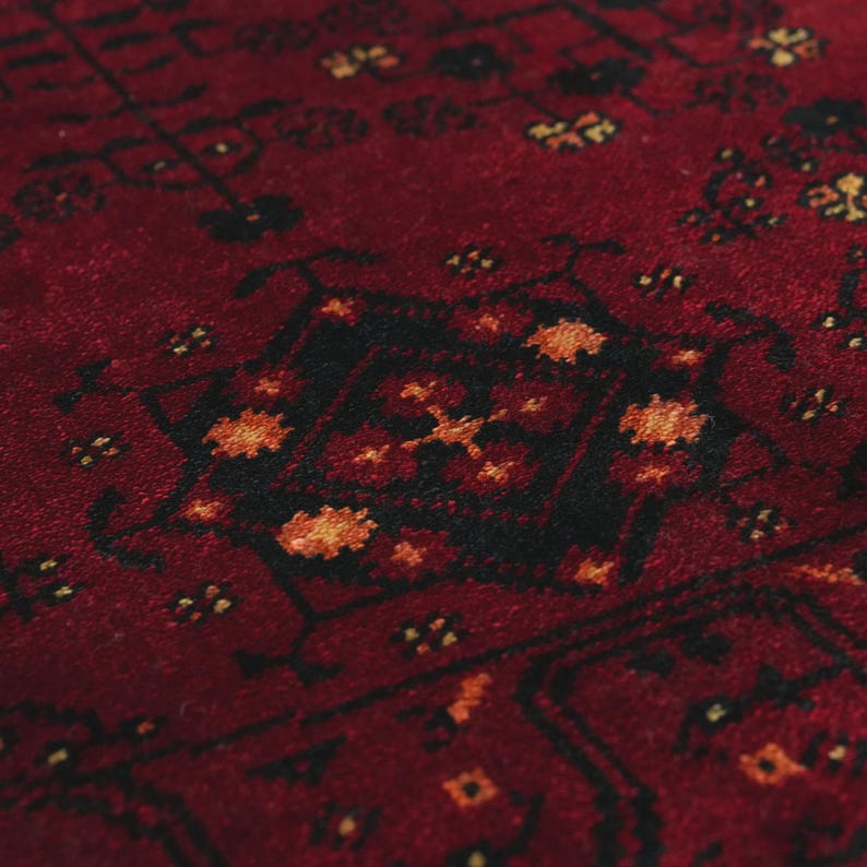 May include: Close-up of a red rug with a detailed pattern. The rug features a central black design with orange and yellow accents, surrounded by smaller floral motifs. The texture appears soft and plush.