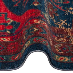 May include: Close-up of a section of a patterned rug. The rug features a deep blue border with a central design in red, brown, and green. The intricate pattern includes floral and geometric elements, creating a traditional aesthetic.
