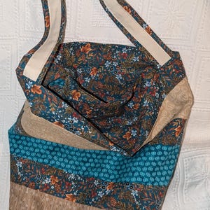 May include: A teal blue and brown patchwork tote bag with a floral print and a white strap. The bag has a wide opening and is made of fabric.