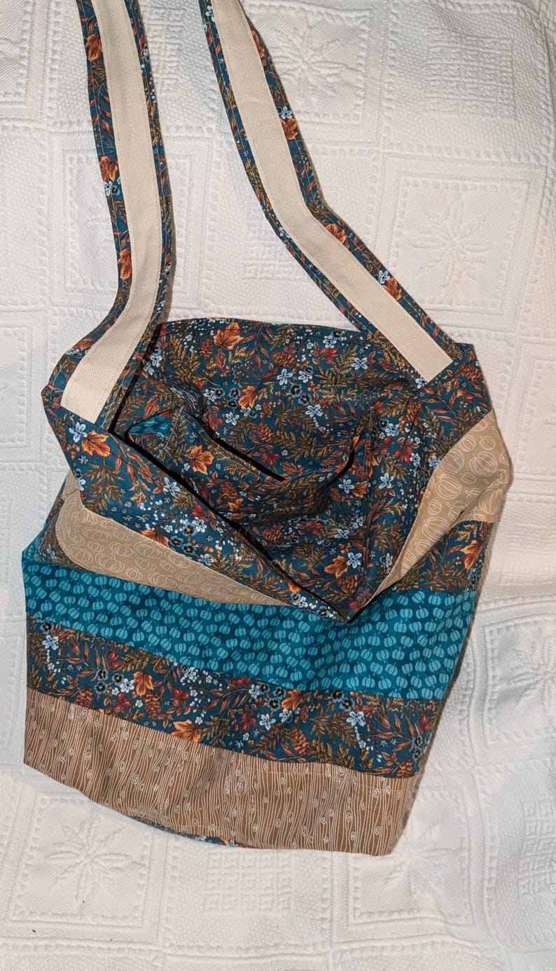May include: A teal blue and brown patchwork tote bag with a floral print and a white strap. The bag has a wide opening and is made of fabric.
