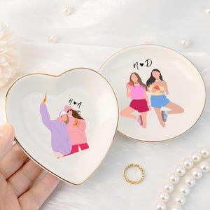 Pu&ograve; includere: Due portagioie decorativi in ceramica. Uno &egrave; a forma di cuore, l'altro rotondo. Entrambi hanno un bordo dorato e presentano illustrazioni di persone. Il piatto a forma di cuore ha le lettere "H&bull;A". Il piatto rotondo ha le lettere "N&bull;D".