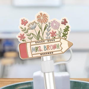 May include: Wooden pencil-shaped sign with a red eraser and a floral design. The sign says "MRS. BROWN" in brown lettering.