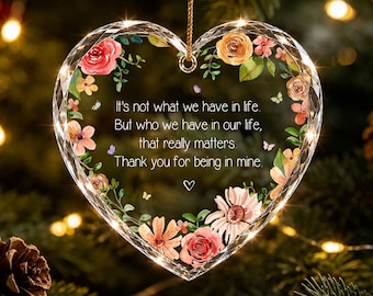 Op de afbeelding: Een hartvormig, transparant acryl ornament met een bloemenrand van roze, oranje en gele bloemen en kleine vlinders. De tekst luidt: It's not what we have in life, But who we have in our life, that really matters. Thank you for being in mine.