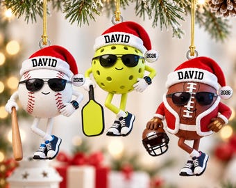May include: Three hanging ornaments featuring a baseball, a pickleball, and a football, each wearing a red Santa hat with the name DAVID and the year 2026. Each character wears black sunglasses, sneakers, and holds a sports item like a bat or helmet.