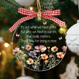 Op de afbeelding: Een rond, transparant acryl ornament met een rood-wit geblokte strik aan de bovenkant. De tekst luidt: It's not what we have in life. But who we have in our life, that really matters. Thank you for being in mine. Versierd met bloemen en vlinders.