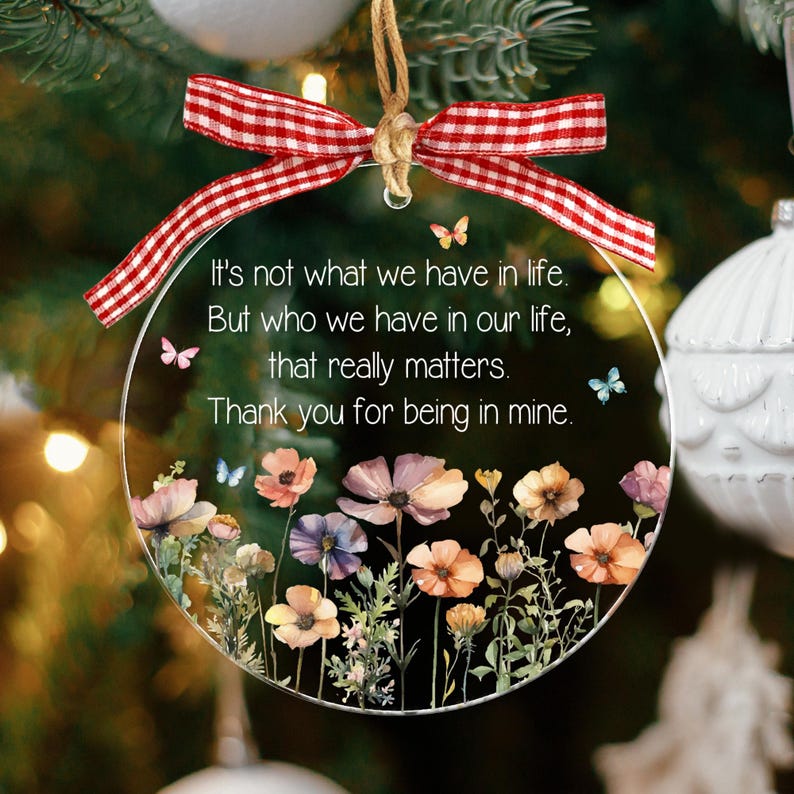 Op de afbeelding: Een rond, transparant acryl ornament met een rood-wit geblokte strik aan de bovenkant. De tekst luidt: It's not what we have in life. But who we have in our life, that really matters. Thank you for being in mine. Versierd met bloemen en vlinders.