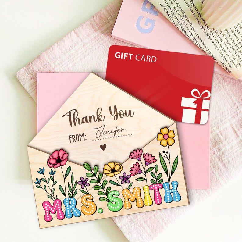 May include: A wooden envelope with a floral design and the text "Thank You" and "MRS. SMITH". The envelope is open and a red gift card is visible inside.