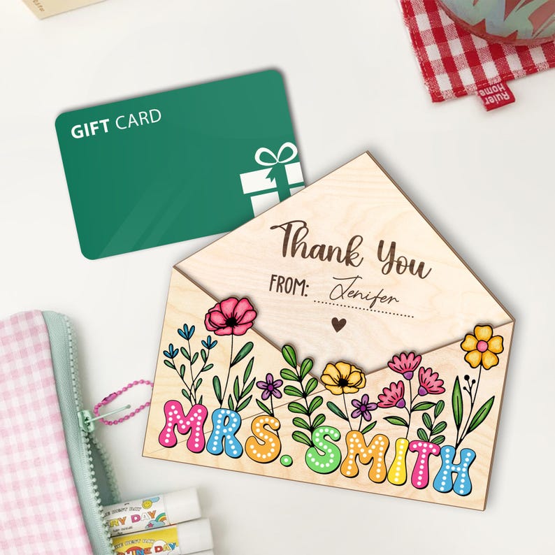 May include: Wooden gift card holder with a floral design and the text "Thank You" and "From: Jennifer". The holder has a cutout for a gift card and the words "Mrs. Smith" are spelled out in colorful letters.