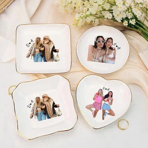 Pu&ograve; includere: Quattro piattini in ceramica bianca con bordi dorati. Ogni piatto presenta una foto diversa di due persone. I piatti sono quadrati, rotondi e a forma di cuore. Un anello d'oro si trova vicino al piatto a forma di cuore. I piatti sono su una superficie bianca.