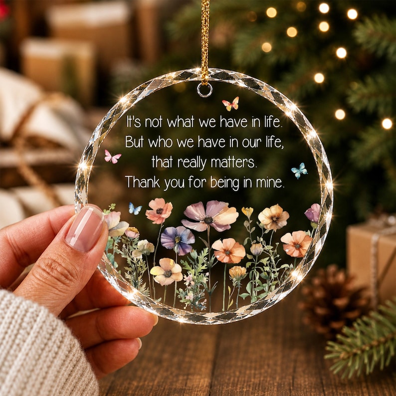 May include: A circular clear acrylic ornament with a faceted edge, featuring a printed floral design of colorful wildflowers and small butterflies. The text reads: It's not what we have in life, But who we have in our life, that really matters. Thank you for being in mine.
