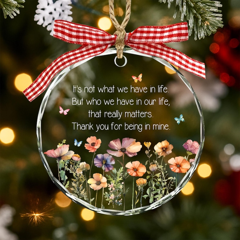 Op de afbeelding: Een rond glazen ornament met een rood-wit geblokte strik aan de bovenkant. In het midden staat de tekst: It's not what we have in life, But who we have in our life, that really matters. Thank you for being in mine, versierd met bloemen.