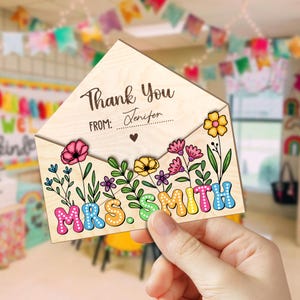 May include: Wooden thank you card with a floral design and the text "Thank You" and "From:" with a space for a name. The card is shaped like an envelope and has the name "MRS. SMITH" in colorful letters.