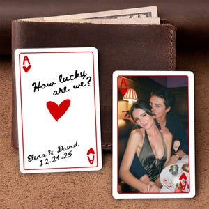 May include: Two playing cards with a red border. One card has the text "How lucky are we?" with a red heart and the names "Elena & David" and the date "12.24.25". The other card has a photo of a couple.