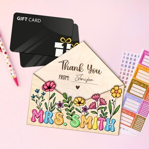 May include: A wooden thank you card with a floral design and the text "Thank You" and "MRS. SMITH". The card is shaped like an envelope and has a gift card tucked inside.