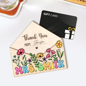 May include: Wooden gift card holder with a floral design and the text "Thank You Jennifer" and "Mrs. Smith". The holder is shaped like an envelope and has a slot for a gift card.
