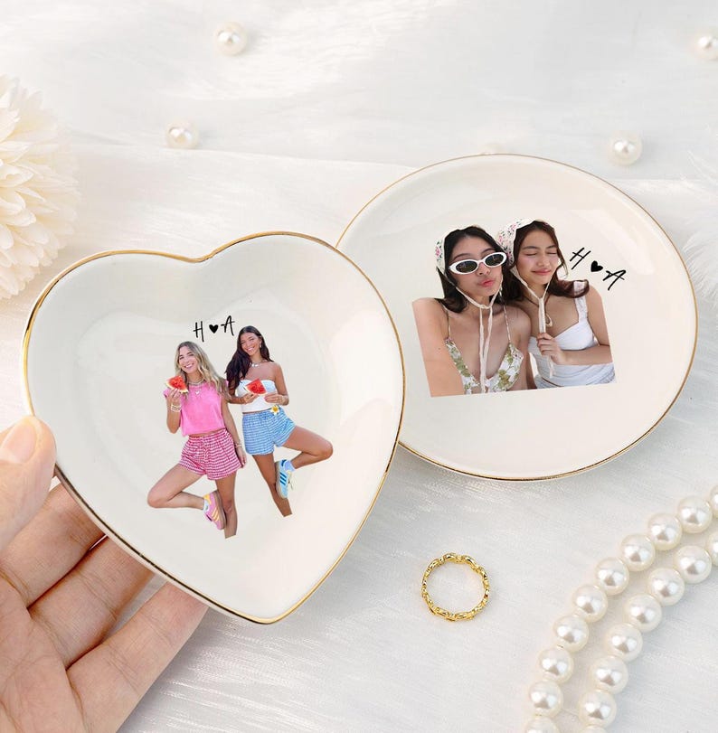 Pu&ograve; includere: Due portagioie in ceramica, uno a forma di cuore e uno rotondo, con bordi dorati. Il piatto a forma di cuore presenta una foto di due donne, le iniziali "H ❤️ A" e un anello d'oro. Il piatto rotondo ha una foto di due donne e le iniziali "H ❤️ A".