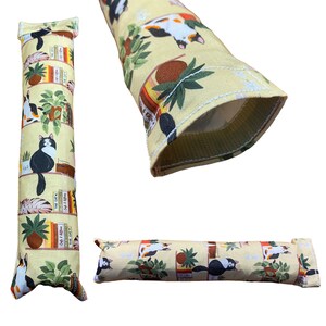 May include: A yellow cat toy with a cat and books print. The toy is a long, thin cylinder with a hole in the middle. The toy is made of fabric and has a white seam around the edge.