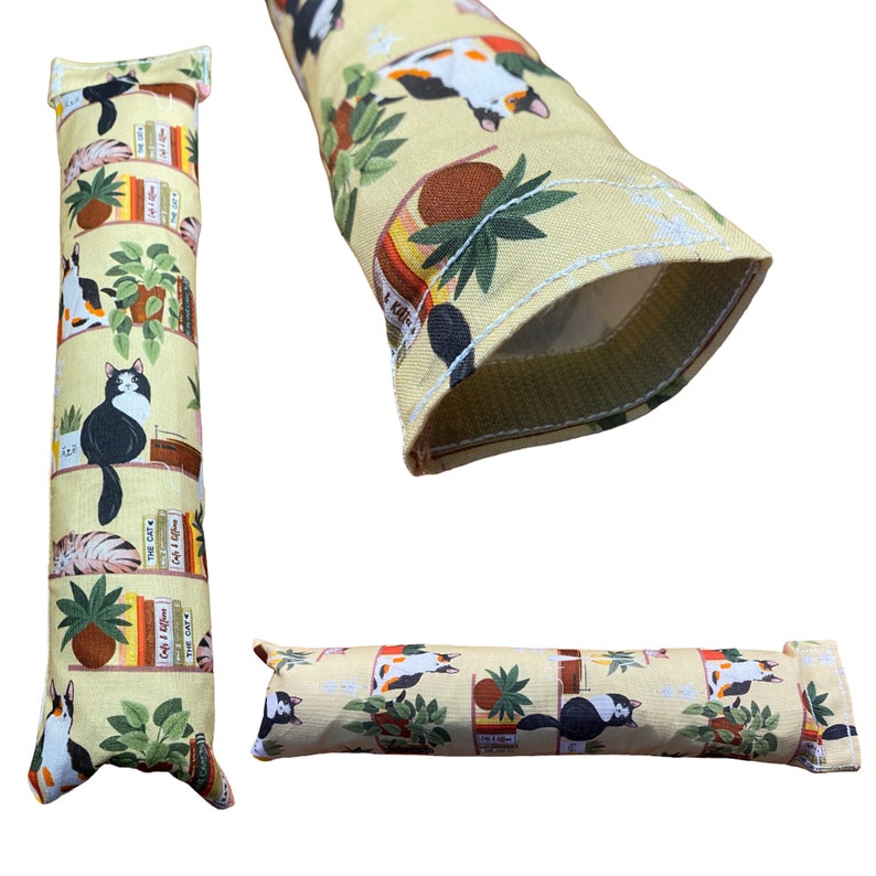 May include: A yellow cat toy with a cat and books print. The toy is a long, thin cylinder with a hole in the middle. The toy is made of fabric and has a white seam around the edge.