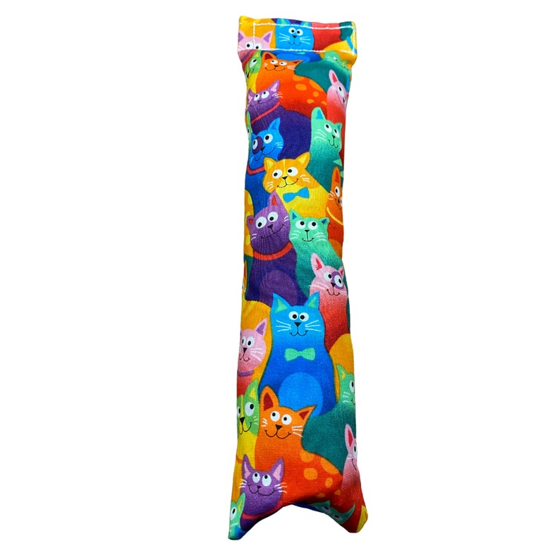 May include: A long, rectangular catnip toy with a colorful print of cats in various colors and poses. The toy is made of fabric and has a sewn seam down the center.