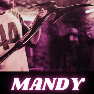 May include: A movie poster for the film Mandy, featuring Nicolas Cage holding a large, black axe. The title "MANDY" is in pink neon letters. The text "A FILM BY PANOS COSMATOS" is below the title. The names "NICOLAS CAGE", "ANDREA RISEBOROUGH", and "LINUS ROACHE" are listed below the director's name.