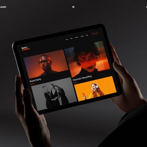 K&ouml;nnte beinhalten: Ein schwarzes Tablet, das eine Website mit dem Text "Aura Creative" und verschiedenen Bildminiaturen anzeigt. Die Miniaturen zeigen Personen und den Text "Brand Clarity" und "Cinematic Storytelling". Das Tablet wird vor einem dunklen Hintergrund gehalten.