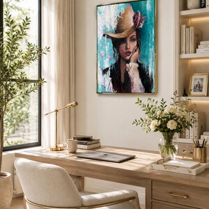 May include: A rectangular wall art piece featuring a portrait of a person wearing a wide-brimmed hat, rendered in textured brushstrokes. The color palette includes shades of teal, white, black, and brown, with a gold frame surrounding the canvas.
