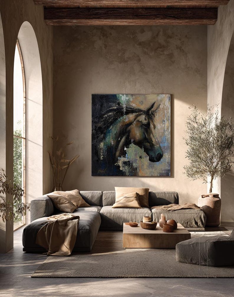 May include: A square wall art painting featuring a dark, textured profile of a horse head in shades of brown, black, and blue. The artwork is displayed on a neutral-toned wall above a low-profile grey sectional sofa with tan cushions.