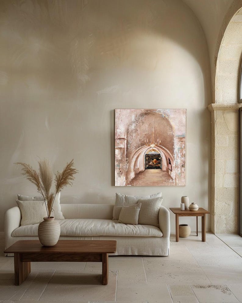 May include: A square canvas painting depicting a stone archway with a hanging chandelier and a dark interior passage. The artwork features textured brushstrokes in shades of beige, cream, and brown, displayed on a neutral wall above a sofa.