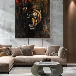 May include: A square wall art piece featuring a detailed tiger face emerging from a dark, textured background with streaks of black, brown, and vibrant orange paint. The artwork is enclosed in a thin, simple frame and mounted on a light wall.